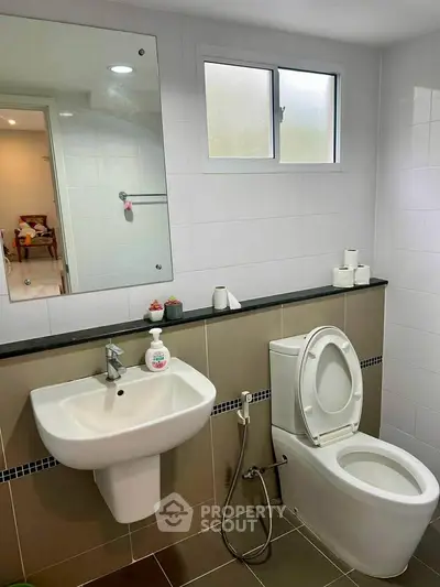 Modern bathroom with sleek fixtures and neutral tiles, featuring a large mirror and window for natural light.