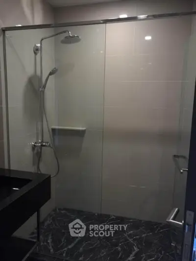 Modern bathroom with sleek glass shower and elegant black marble flooring.