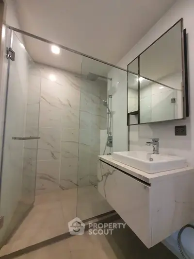 Modern bathroom with sleek glass shower enclosure, marble walls, and a stylish floating vanity sink, perfect for contemporary living.