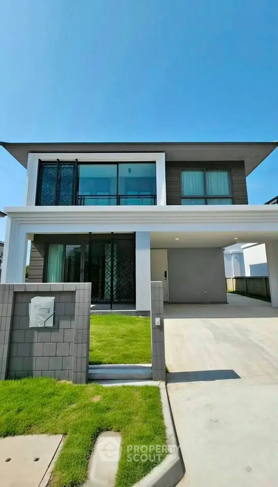 Modern two-story house with sleek design and spacious driveway under clear blue sky.