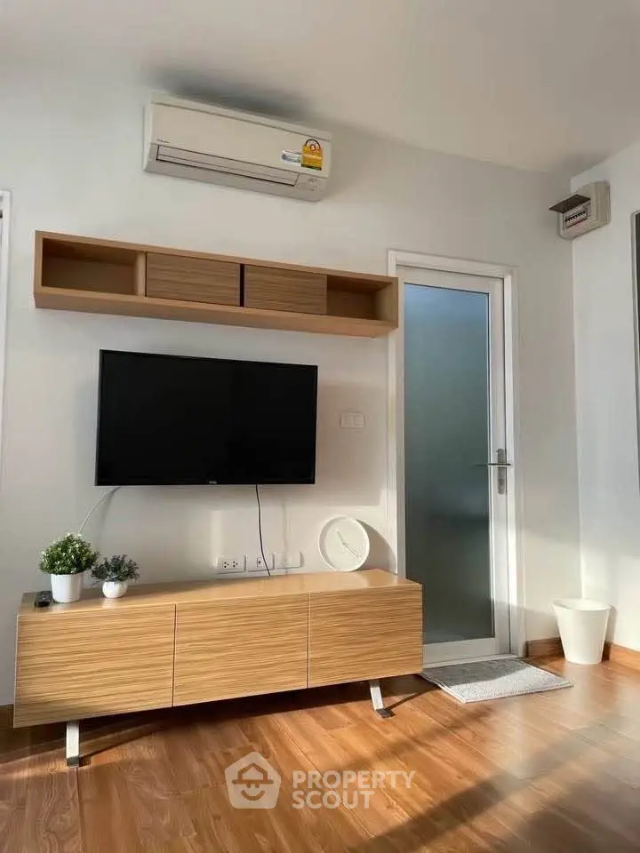 Modern living room with sleek wooden furniture and wall-mounted TV under air conditioning unit.