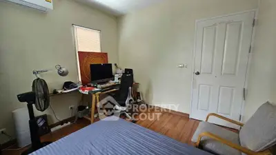 Cozy bedroom with workspace, featuring wooden flooring and natural light.