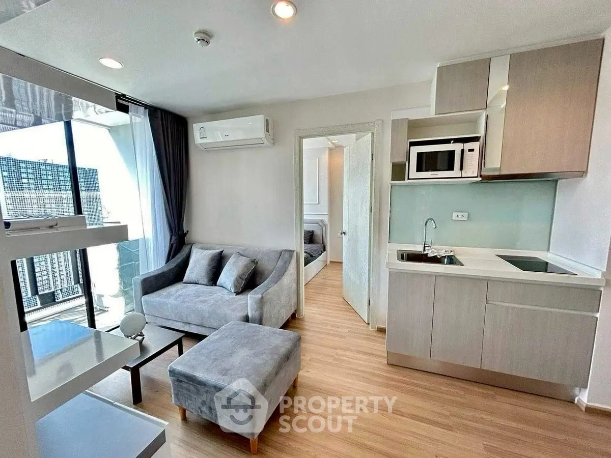 Modern living room with open kitchen and city view, featuring sleek furniture and natural light.