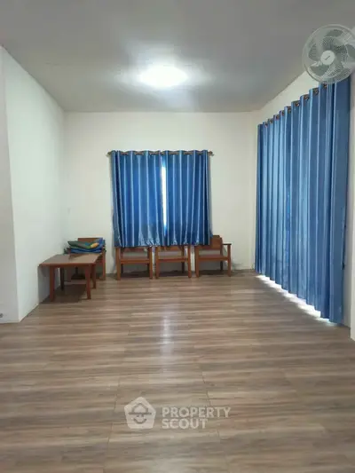Spacious living room with wooden flooring and blue curtains, ideal for cozy gatherings.