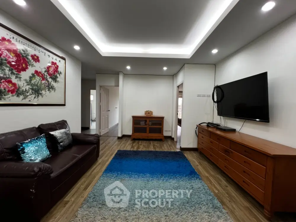 Spacious living room with modern lighting, plush seating, and a large flat-screen TV, complemented by a vibrant area rug and wooden accents.