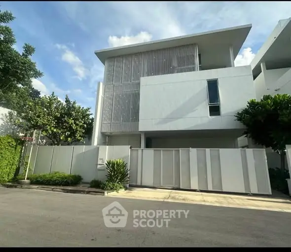 Modern minimalist white house with sleek facade and lush greenery in a serene neighborhood.