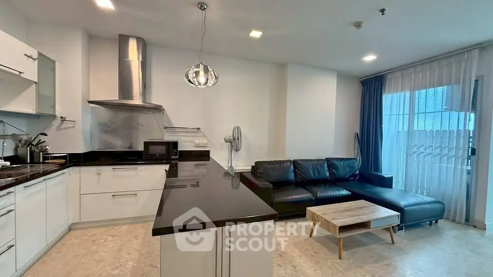 Modern open-layout kitchen and living room with sleek black countertops and cozy seating area.