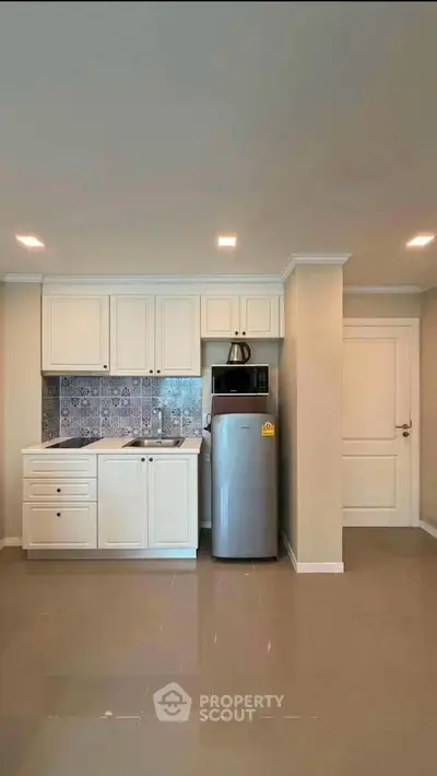Modern kitchen with sleek cabinetry and stainless steel fridge in a cozy apartment.