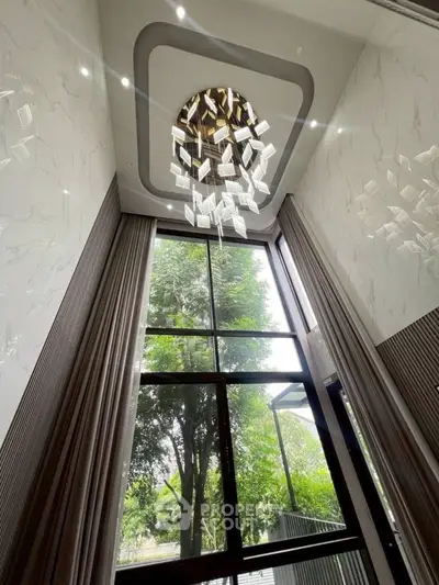 Luxurious high-ceiling living room with stunning chandelier and large windows overlooking greenery.