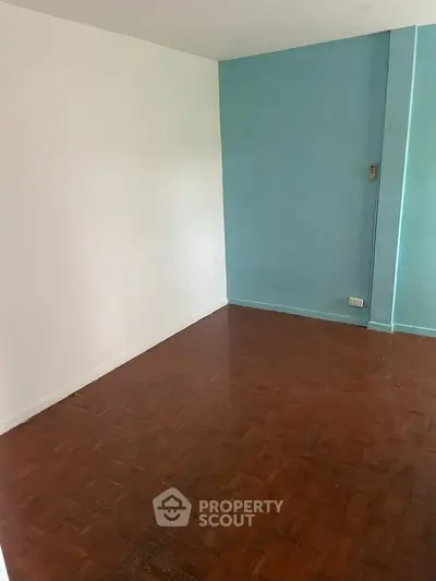 Spacious empty room with parquet flooring and blue accent wall, ideal for customization.