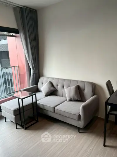 Modern living room with stylish gray sofa and glass coffee table near balcony.