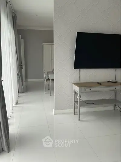 Modern living room with sleek white tiles and wall-mounted TV, featuring elegant furniture and natural light.