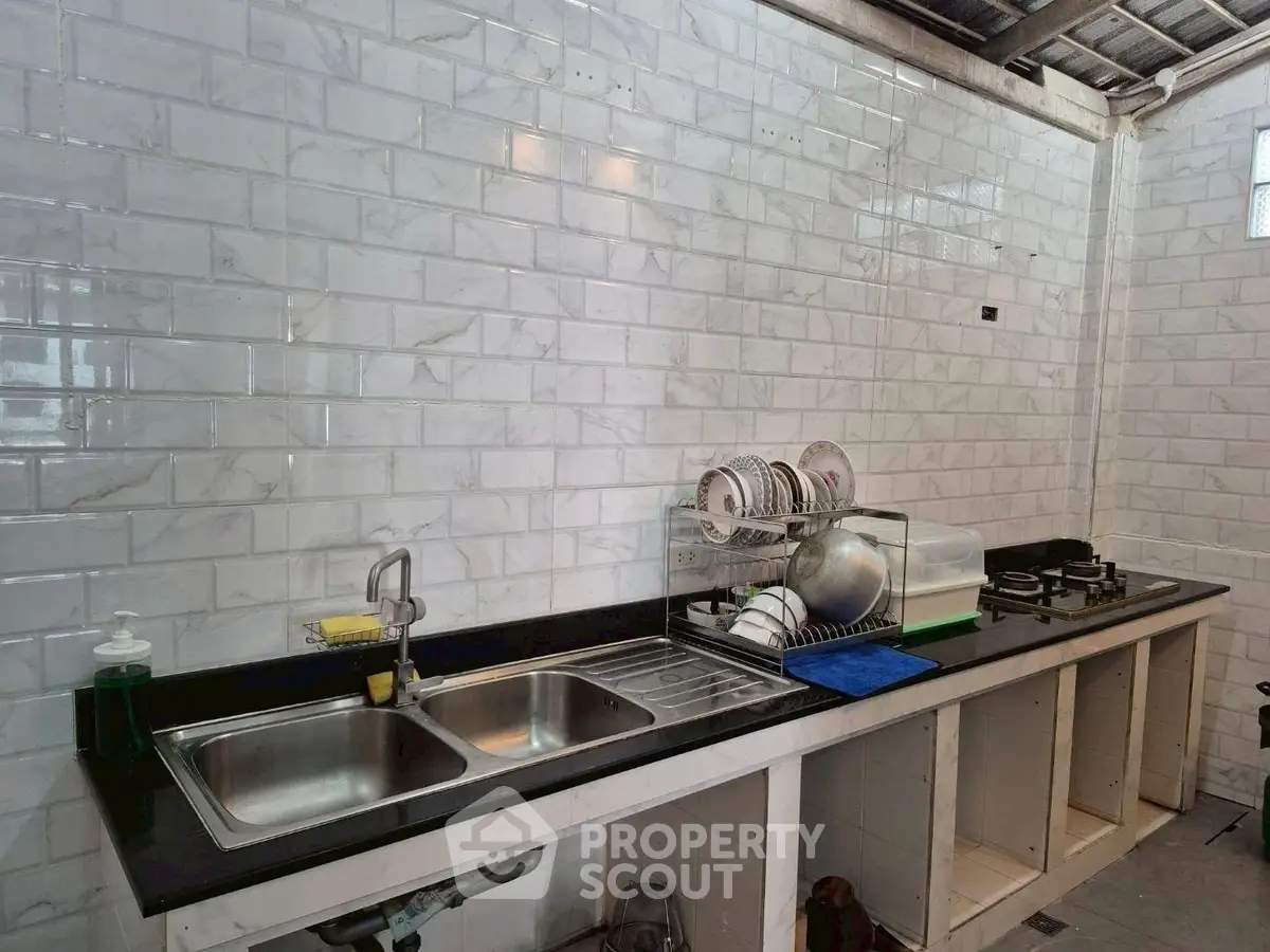 Spacious kitchen with modern sink and gas stove, featuring sleek white tile backsplash.