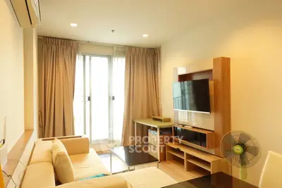 Modern living room with cozy beige sofa and large TV, featuring natural light from balcony window.