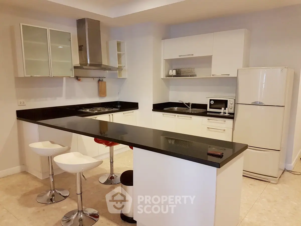 Modern kitchen with sleek black countertops and white cabinetry, featuring a breakfast bar and stainless steel appliances.