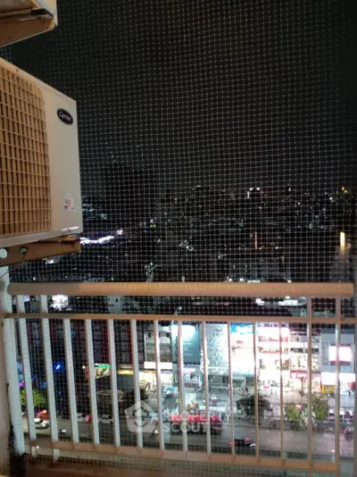 Stunning night city view from a high-rise balcony with safety netting and air conditioning unit.