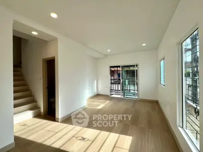 Spacious living room with natural light and modern flooring, featuring a staircase and sliding glass doors.
