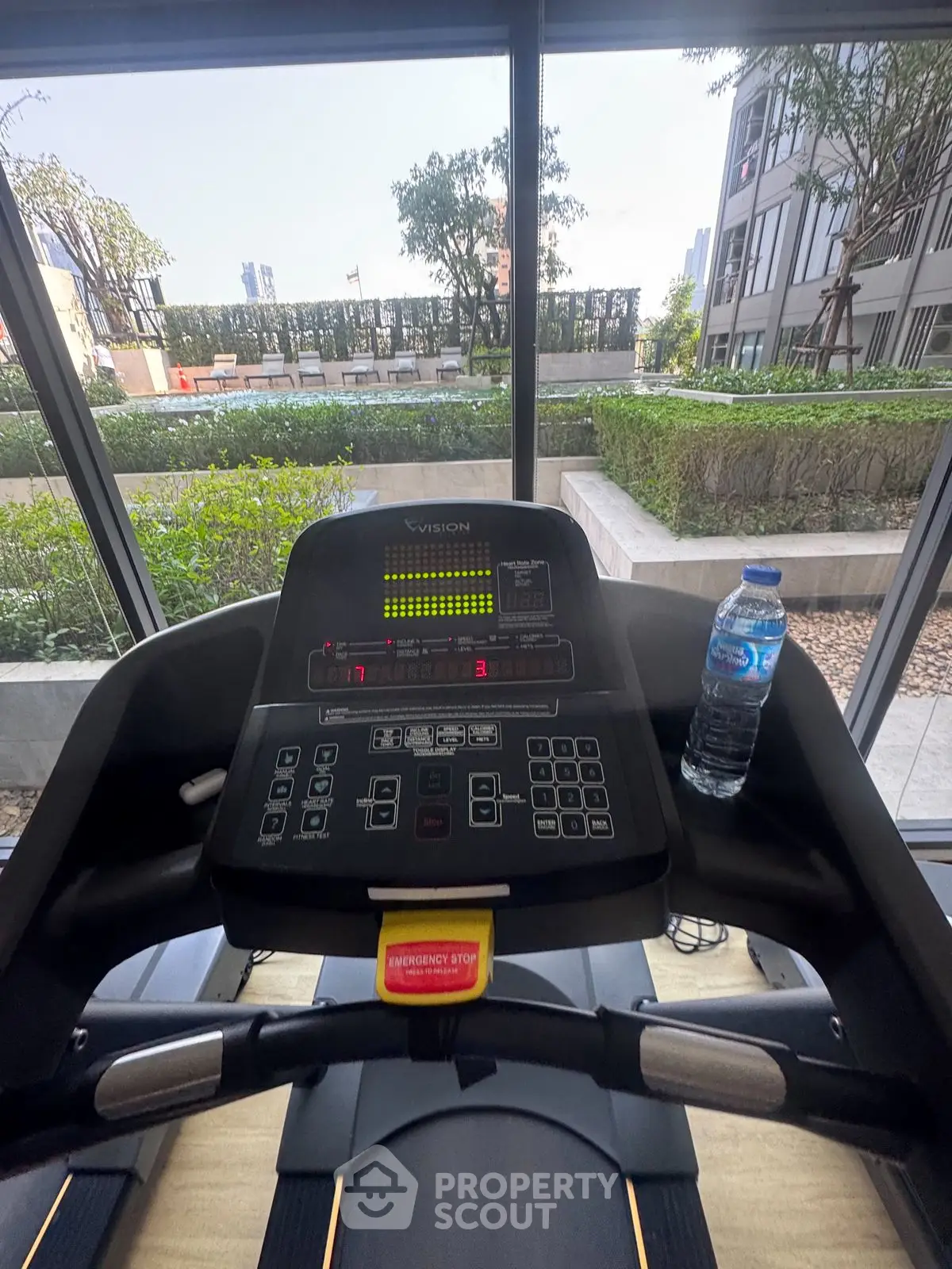 Modern gym with treadmill overlooking lush garden and cityscape view.