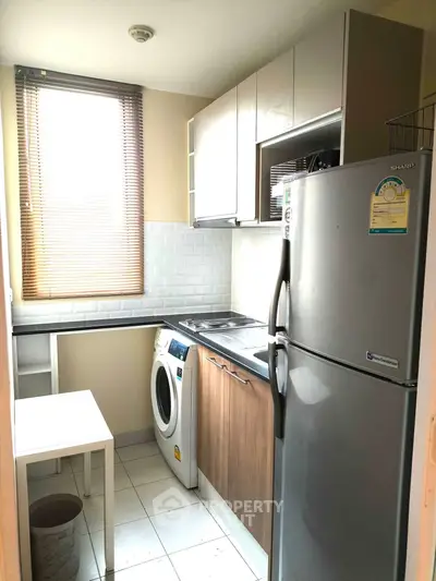 Compact kitchen with modern appliances, washing machine, and ample natural light from large window.