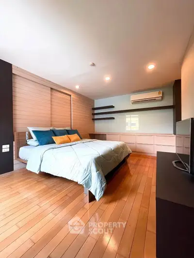 Spacious bedroom with wooden flooring and modern decor, featuring a cozy bed and air conditioning.