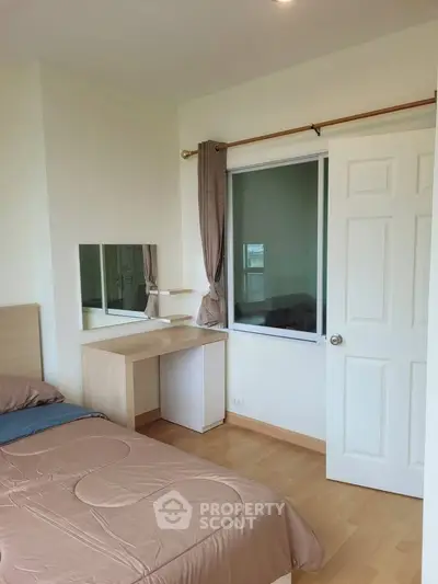 Cozy bedroom with wooden flooring and natural light, featuring a single bed and a small desk.