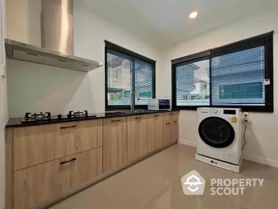 Modern kitchen with sleek cabinets and washing machine, featuring gas stove and ample natural light.