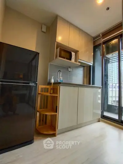 Modern kitchen with sleek cabinets, microwave, and large fridge in a bright apartment with balcony view.