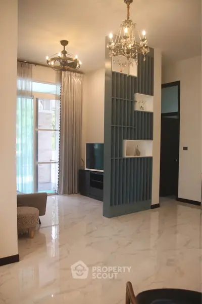 Elegant living room with modern chandelier and stylish shelving, featuring marble flooring and natural light.