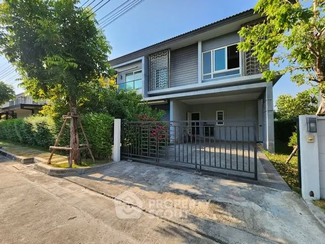 Modern two-story house with gated driveway and lush greenery in a serene neighborhood.