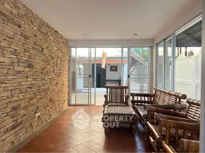 Charming sunlit room with rustic stone wall and bamboo furniture, perfect for relaxation.