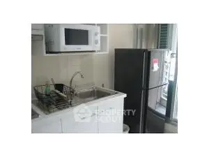 Compact kitchen with microwave, sink, and refrigerator in modern apartment.
