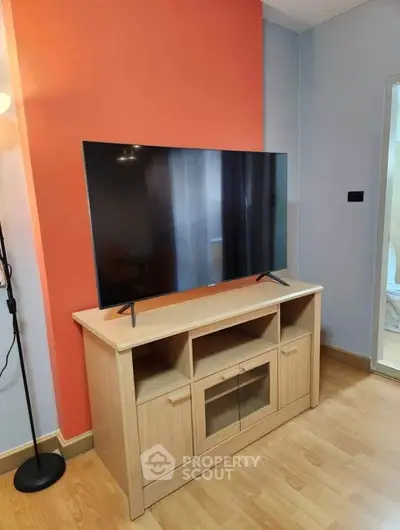 Modern living room with sleek TV on wooden stand and vibrant orange accent wall.