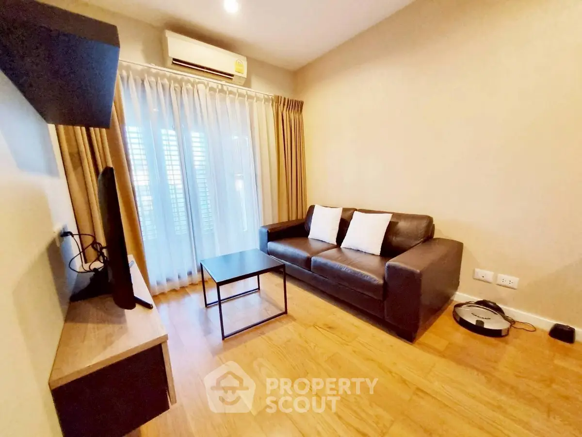 Cozy living room with modern sofa and TV, featuring wooden flooring and natural light.