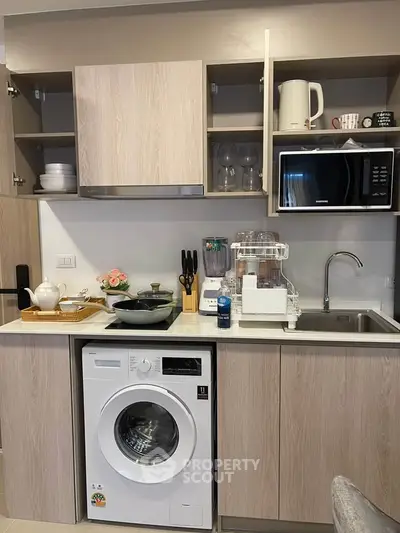 Modern kitchen with washing machine, microwave, and open cabinets showcasing sleek design.