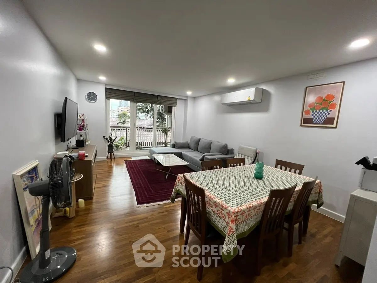 Spacious living room with modern decor and dining area, featuring hardwood floors and natural light.