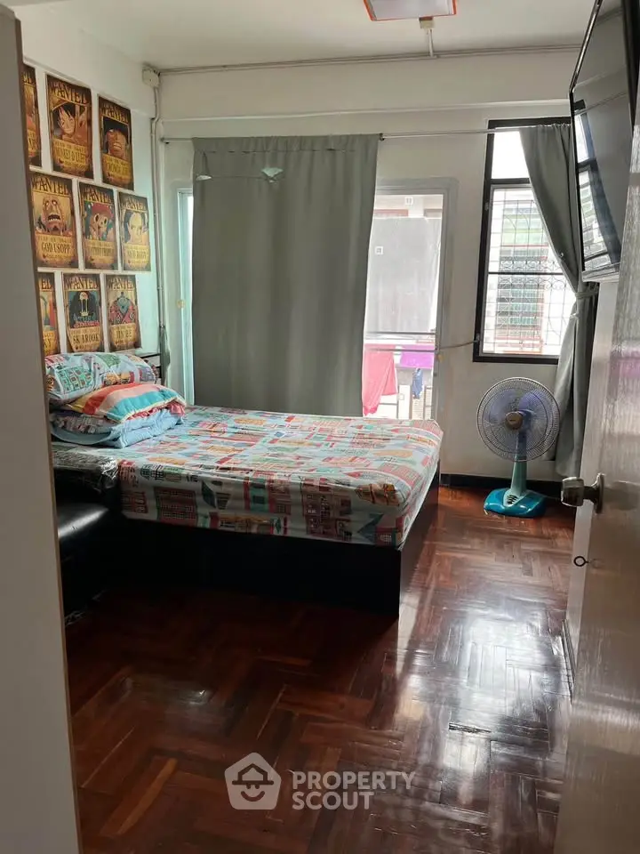 Cozy bedroom with wooden flooring and vintage posters, featuring a comfortable bed and natural light.