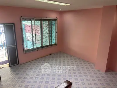 Spacious pink-walled room with patterned tile flooring and large window, perfect for versatile living space.