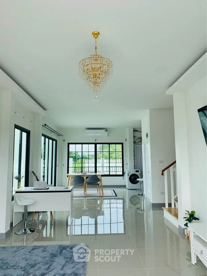 Spacious and bright living area with gleaming floor tiles, elegant chandelier, and modern furnishings, leading to a cozy dining space.
