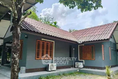 Charming single-story home with tiled roof and air conditioning units, surrounded by lush greenery.