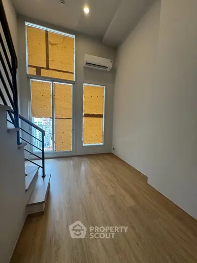 Spacious modern living room with large windows and wooden flooring in a high-rise apartment.