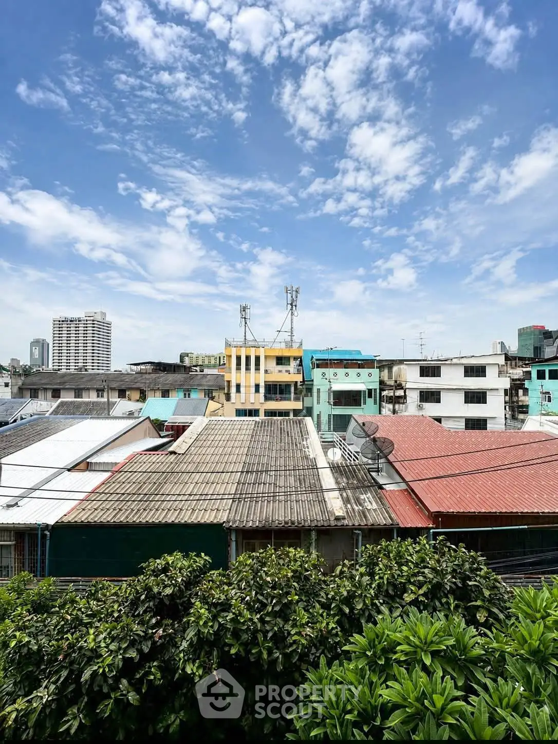 Urban skyline view with diverse rooftops and lush greenery under a clear blue sky.