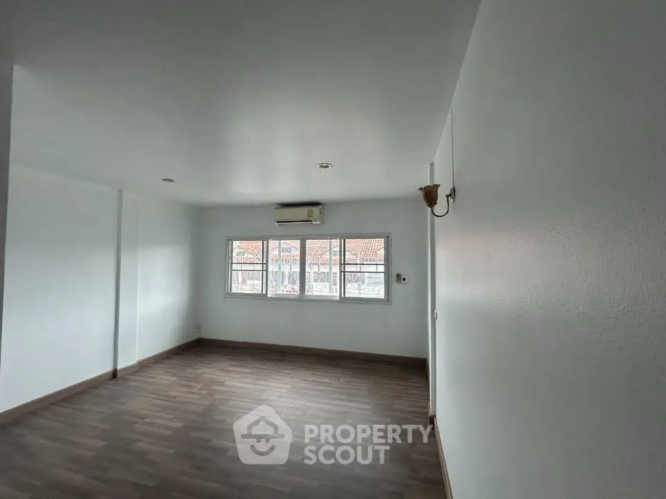 Spacious empty room with wooden flooring and large windows, perfect for customization.