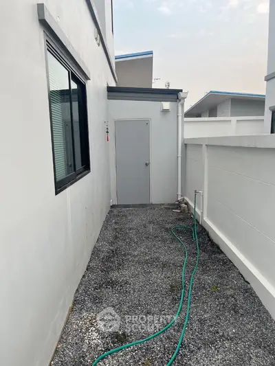 Modern exterior side path with gravel and hose, leading to a sleek door, ideal for urban living.