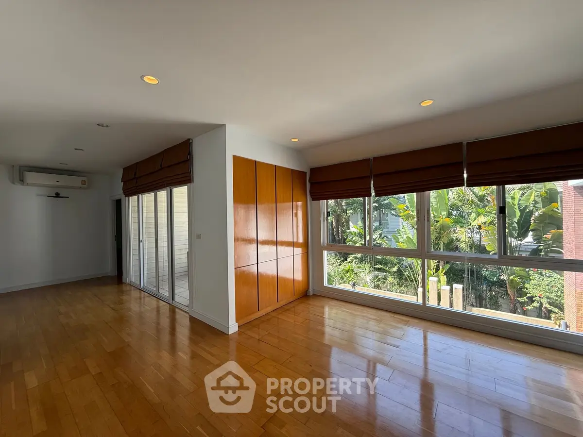 Spacious living room with large windows and wooden flooring, offering a serene garden view.