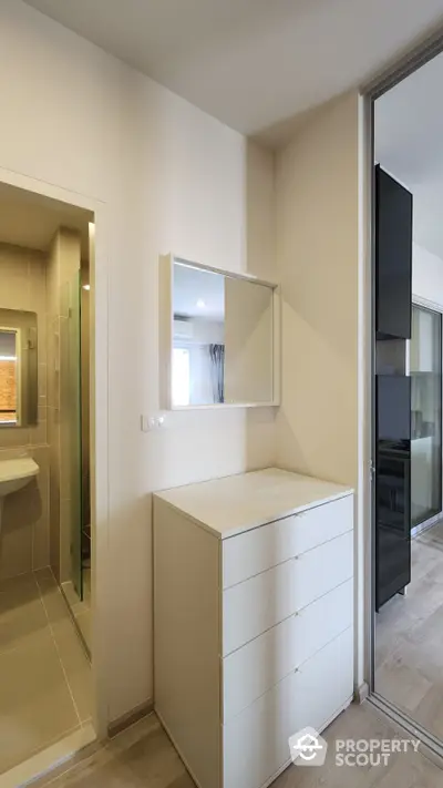 Modern minimalist bedroom with sleek white furnishings and ample natural light, featuring a large mirror and a view into a stylish bathroom.