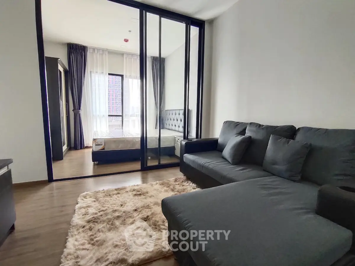 Modern living room with cozy sofa and glass partition leading to bedroom, featuring elegant decor.