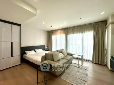 Modern studio apartment with cozy living area and large windows for natural light.