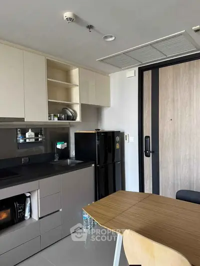 Modern compact kitchen with sleek cabinetry and dining area in contemporary apartment.