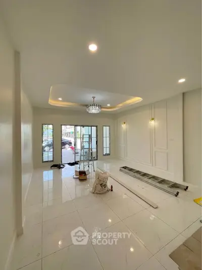Spacious modern living room with elegant chandelier and large windows, perfect for natural light.