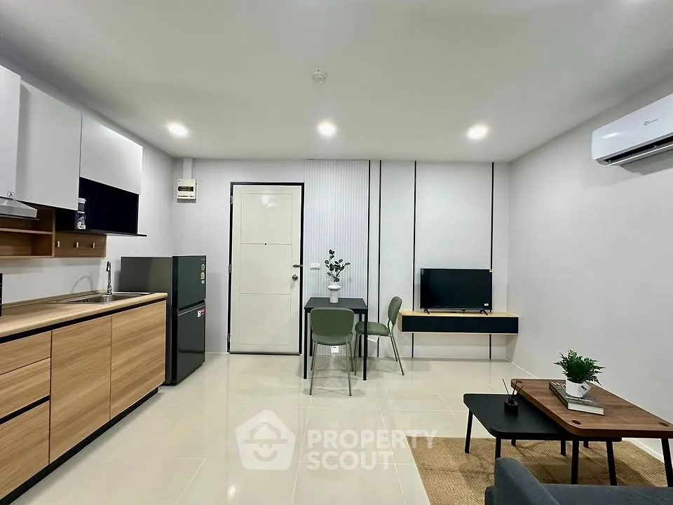 Modern open-layout living room with sleek kitchen and dining area, featuring minimalist decor and neutral tones.